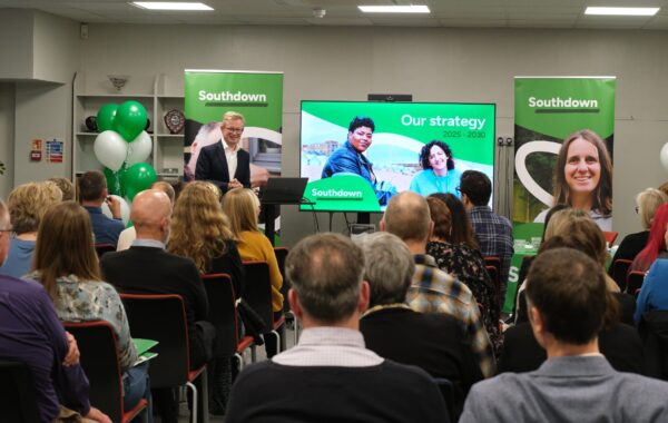 Southdown Chief Executive presenting the new Strategy 2025–2030 at the launch event in Lewes, with colleagues, clients and partners in attendance. A large screen displays the strategy branding alongside Southdown banners and balloons.