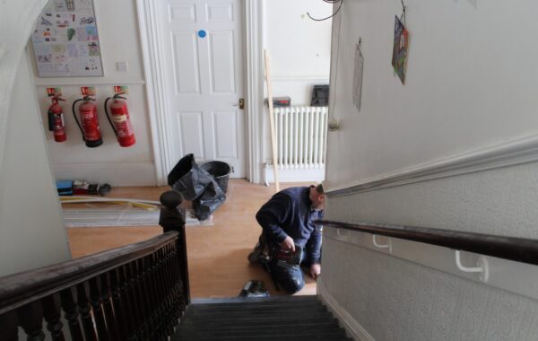 A maintenance worker carrying out repairs in a residential building hallway, representing efforts to improve housing conditions under Awaab’s Law.