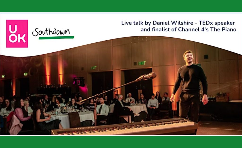 Promotional banner for a live talk on mental health awareness by Daniel Wilsher, TEDx speaker and finalist of Channel 4’s The Piano. The image shows Daniel on stage in front of a seated audience, with a microphone and keyboard in the foreground. The UOK and Southdown logos are displayed at the top of the banner. The talk's theme is - Building community through service.