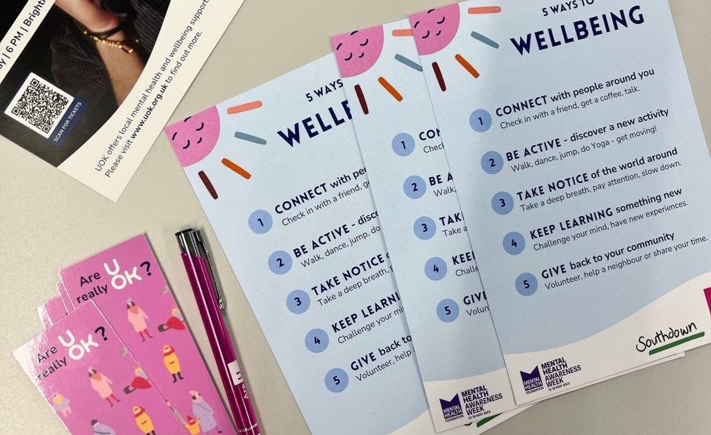 Promotional materials from the UOK event for Mental Health Awareness Week, including wellbeing tip cards, UOK leaflets, pens, mints, and bookmarks encouraging mental health check-ins.