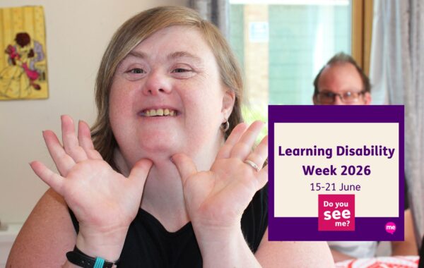A smiling woman with a learning disability looks directly at the camera, holding her hands up beside her face in a cheerful pose. Another person is softly out of focus in the background. A purple graphic overlay reads “Learning Disability Week 2026, 15–21 June” alongside the campaign message “Do you see me?”.