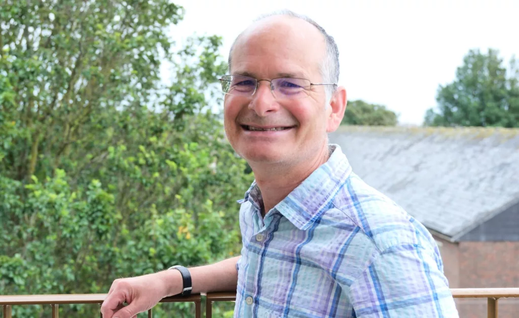Jonathan Senker, Southdown’s incoming Chair, smiles beside an outdoor railing, with trees and a building in the background.