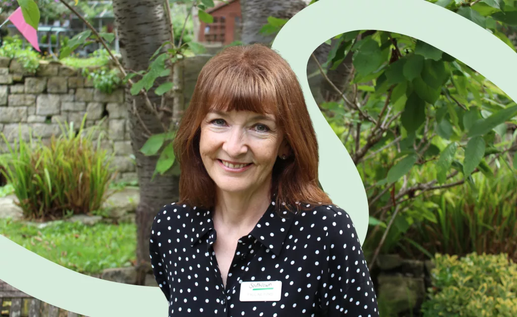 Portrait of Pauline Ford standing in a garden setting, wearing a black polka-dot blouse and Southdown name badge.