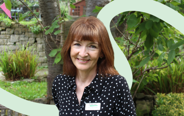 Portrait of Pauline Ford standing in a garden setting, wearing a black polka-dot blouse and Southdown name badge.